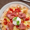 Pizza con prosciutto, pomodorini e burrata su un piatto bianco, accompagnata da una forchetta.