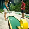 Due persone giocano a minigolf su un percorso illuminato di notte.