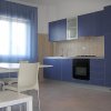 Cucina moderna con mobili blu e tende azzurre, con un tavolo e sedie bianche.