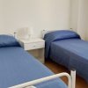 Camera con due letti singoli blu, comodino bianco e lampada.
