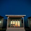 Una casetta in legno al tramonto, con tavolo e sedie in veranda, illuminata da un cielo notturno.