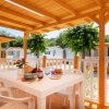 Veranda di legno con tavolo apparecchiato e alberi sullo sfondo.