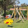 Parco giochi con altalene e giochi a molla, su un prato verde.