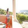 Una persona guarda il paesaggio da una veranda soleggiata, con tavolo e sedia.