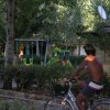 Un uomo in bicicletta passa davanti a un parco giochi con altalene e verde.