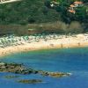 Veduta aerea di una spiaggia affollata con ombrelloni e un mare blu profondo.