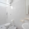 Un bagno con doccia, lavabo, water e bidet, interamente piastrellato in bianco.