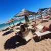 Spiaggia sabbiosa con ombrelloni di paglia e lettini.