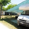 Campeggio con camper bianco parcheggiato sotto una tettoia verde e roulotte sullo sfondo.