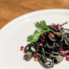Spaghetti al nero di seppia con chicchi di melograno e guarniti con prezzemolo.