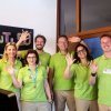 Sei persone in polo verde salutano festosamente davanti a una lavagna.