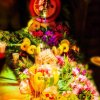 Tavolo decorato con frutta, fiori e luci soffuse, creando un'atmosfera vivace e festosa.