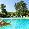 Una piscina all'aperto con una persona su un materassino giallo. Alberi e lettini sullo sfondo.