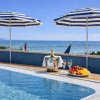Piscina con ombrelloni a strisce, vista mare, e tavolino con frutta e vino.