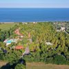 Veduta aerea di un complesso immerso nel verde vicino al mare, con piscine visibili tra gli alberi.