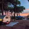 Una roulotte bianca in un campeggio tra gli alberi al tramonto.