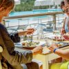 Tre persone pranzano all'aperto con piatti di pesce e bicchieri di vino.