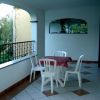 Terrazza con tavolo rotondo coperto da tovaglia rossa e quattro sedie bianche, vista su alberi.