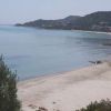 Spiaggia con sabbia chiara e mare tranquillo, colline verdi sullo sfondo.