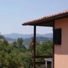 Un edificio beige con un piccolo balcone, circondato da vegetazione e montagne distanti.
