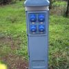 Colonnina blu con prese elettriche all'aperto, situata su erba.