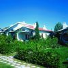 Bungalow bianco con giardino fiorito e vialetto, cielo azzurro.