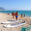 Spiaggia affollata con persone, paddleboard sulla sabbia e mare azzurro.