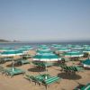 Ombrelloni e sdraio verde acqua su una spiaggia sabbiosa con mare calmo.