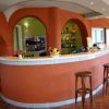Un bancone di bar curvo color terracotta con sgabelli di legno, decorato con bottiglie e tazze.