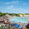 Una grande piscina con molte persone sotto ombrelloni di paglia.