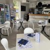 Tavoli e sedie bianche in un bar moderno con frigo e bancone.