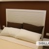 Un letto matrimoniale con testiera bianca e cuscini marroni.