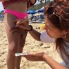 Una donna dipinge un arcobaleno sulla gamba di una ragazza in spiaggia.
