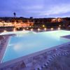 Piscina illuminata di sera con edifici sullo sfondo.