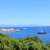 Barca a vela in mare blu con costa rocciosa e cespugli verdi.