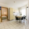 Soggiorno moderno con cucina beige, tavolo e sedie nere. TV appesa e accesso alla camera da letto.