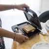 Persona che prepara un toast in una macchina per panini su una tavola apparecchiata.