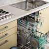Una lavastoviglie aperta in una cucina con piatti e bicchieri caricati, vicino a un lavandino.