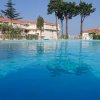 Piscina all'aperto con villette bianche e tetti rossi sullo sfondo, alcune palme e pini.
