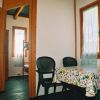 Interno di una casetta in legno con tavolo, sedie verdi, e vista su una camera con letto a castello.