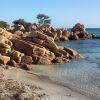 Spiaggia con grandi rocce marroni, sabbia chiara e mare cristallino.