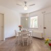 Sala da pranzo con tavolo bianco e fiori. Finestre aperte, pavimento in legno chiaro.
