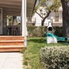 Porticato in legno con tavolo e sedie bianche. Giardino verde vicino a una siepe e un edificio.