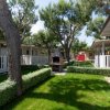 Giardino con barbecue in pietra tra bungalow circondati da siepi e alberi.