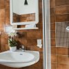 Bagno con piastrelle marroni, lavandino, specchio, doccia e fiori in vaso.