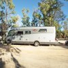 Camper parcheggiato su sterrato tra alberi.