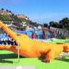 Grande statua di coccodrillo arancione accanto a lettini prendisole e ombrelloni.
