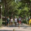 Persone che passeggiano su un viale alberato, con un bambino che corre avanti.