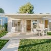 Bungalow moderno con patio, sedie e sdraio su prato verde.