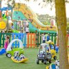 Parco giochi con bambini, automobili giocattolo e uno scivolo gonfiabile colorato.